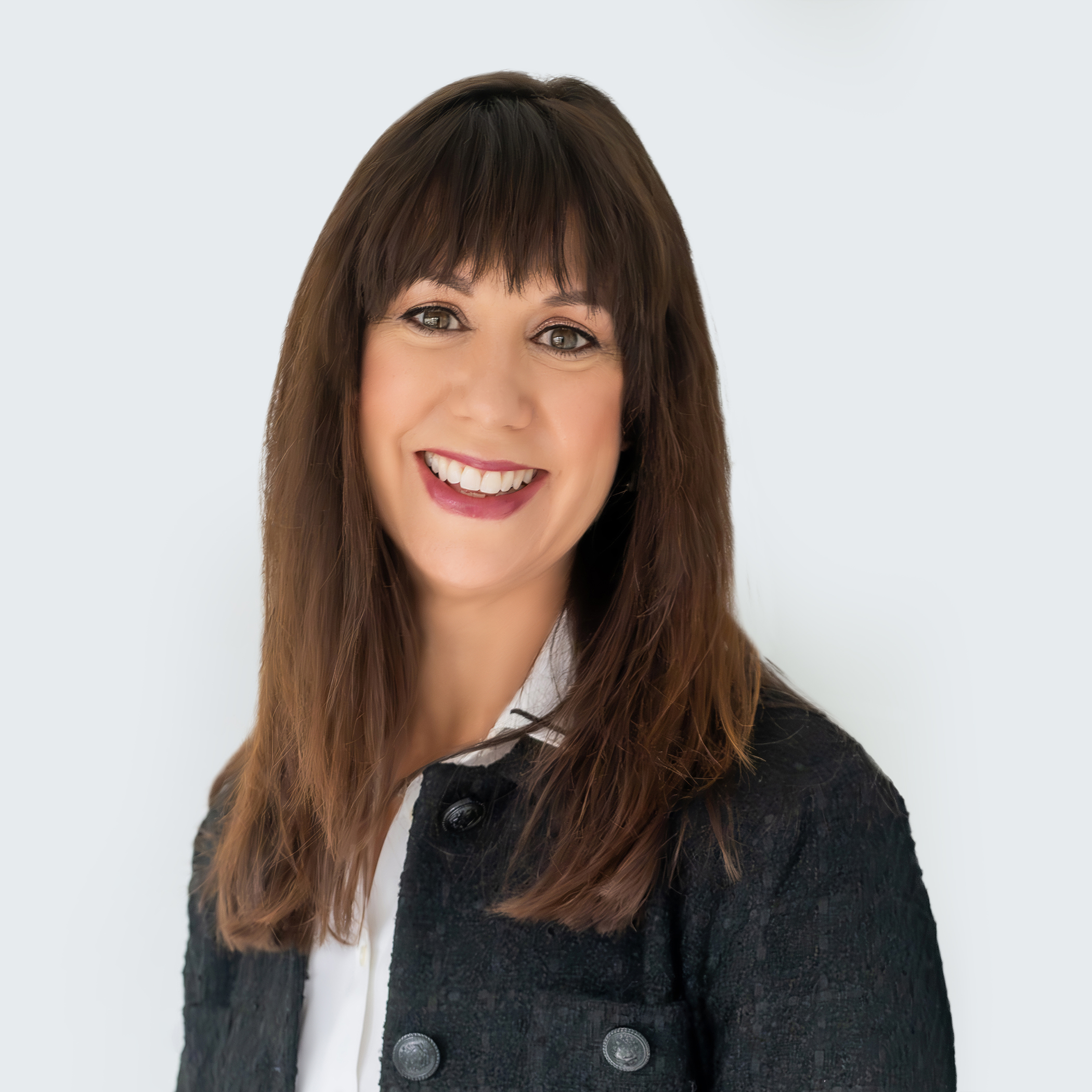 Smiling woman with brown hair and bangs wearing a dark blazer and white top, professional headshot against light gray background.