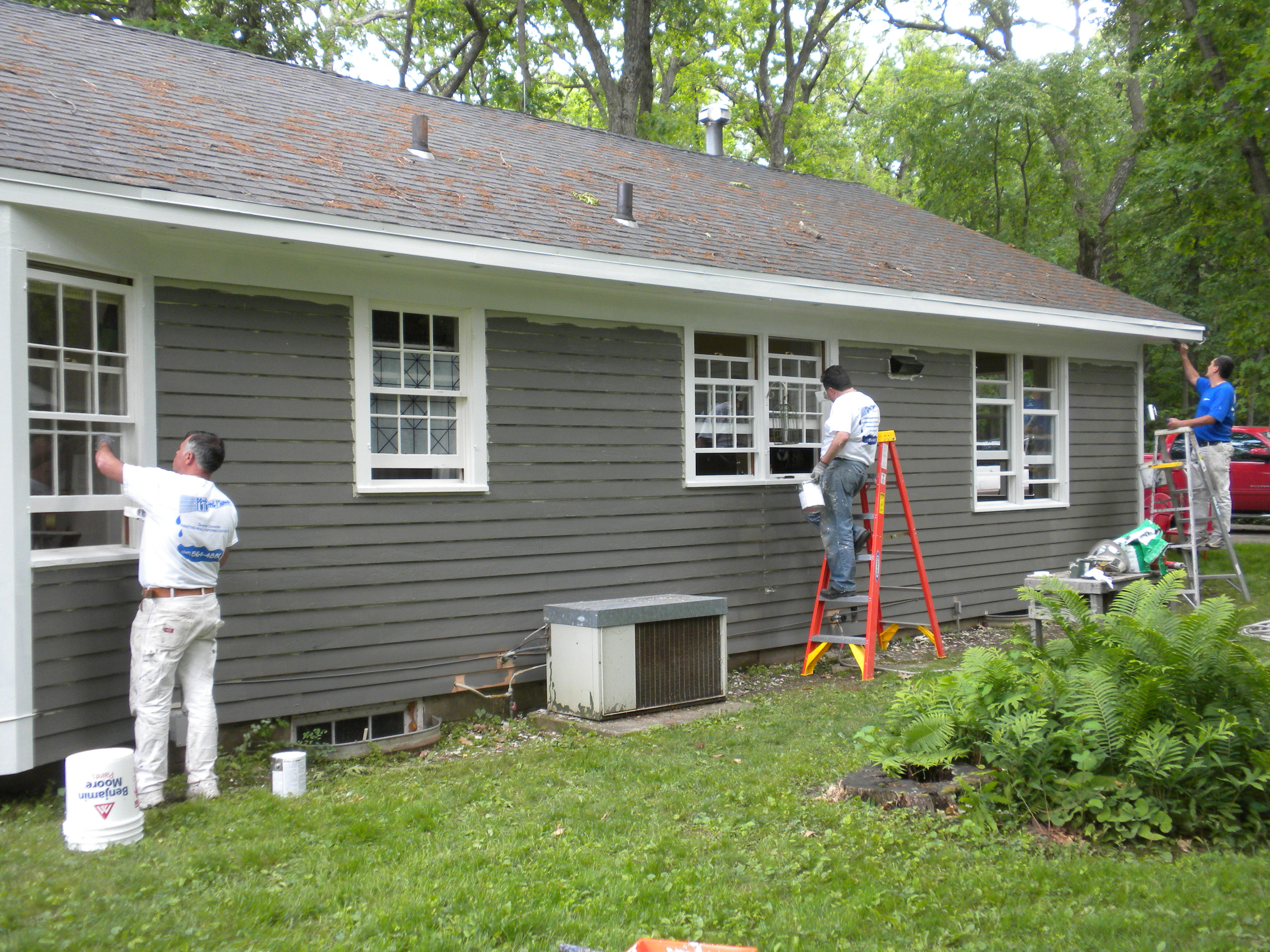 Three Pete the Painter crew members painting the exterior trim and siding of a ranch-style home