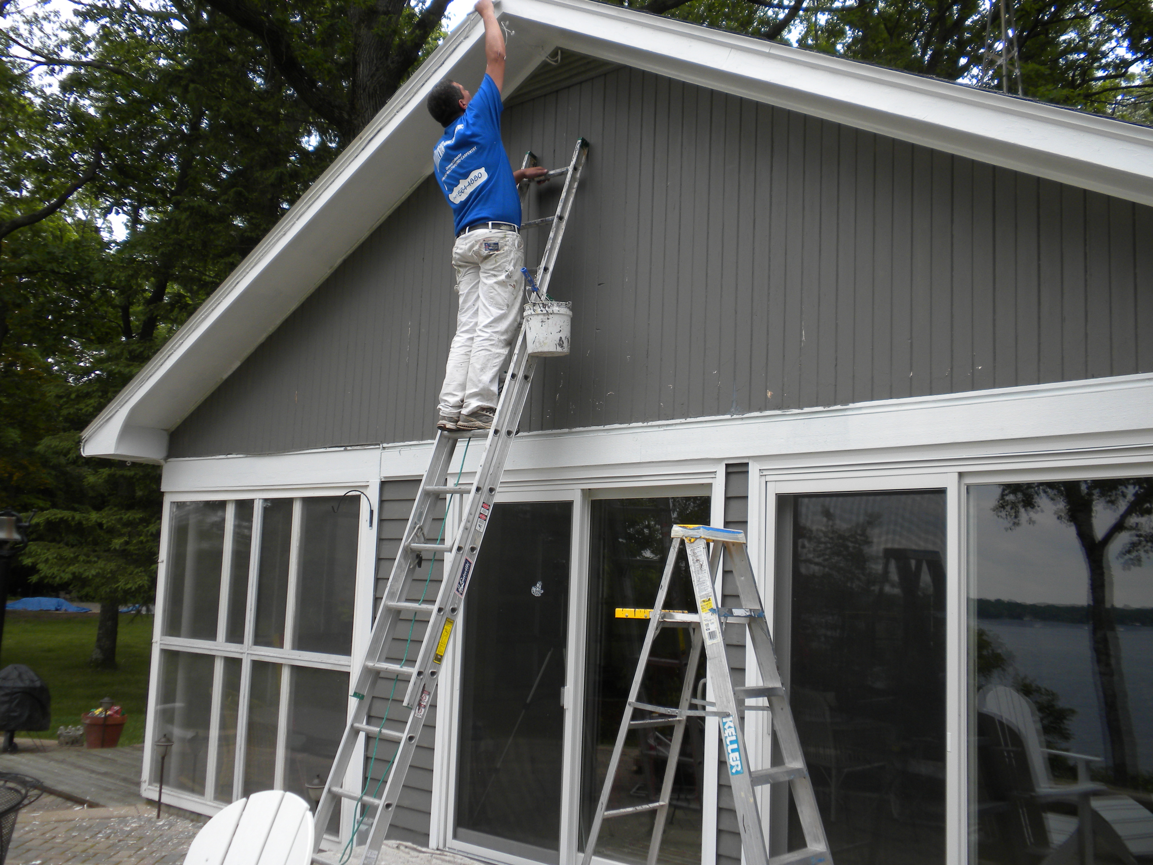 Pete the Painter crew member on an extension ladder painting the upper siding of a lakeside home