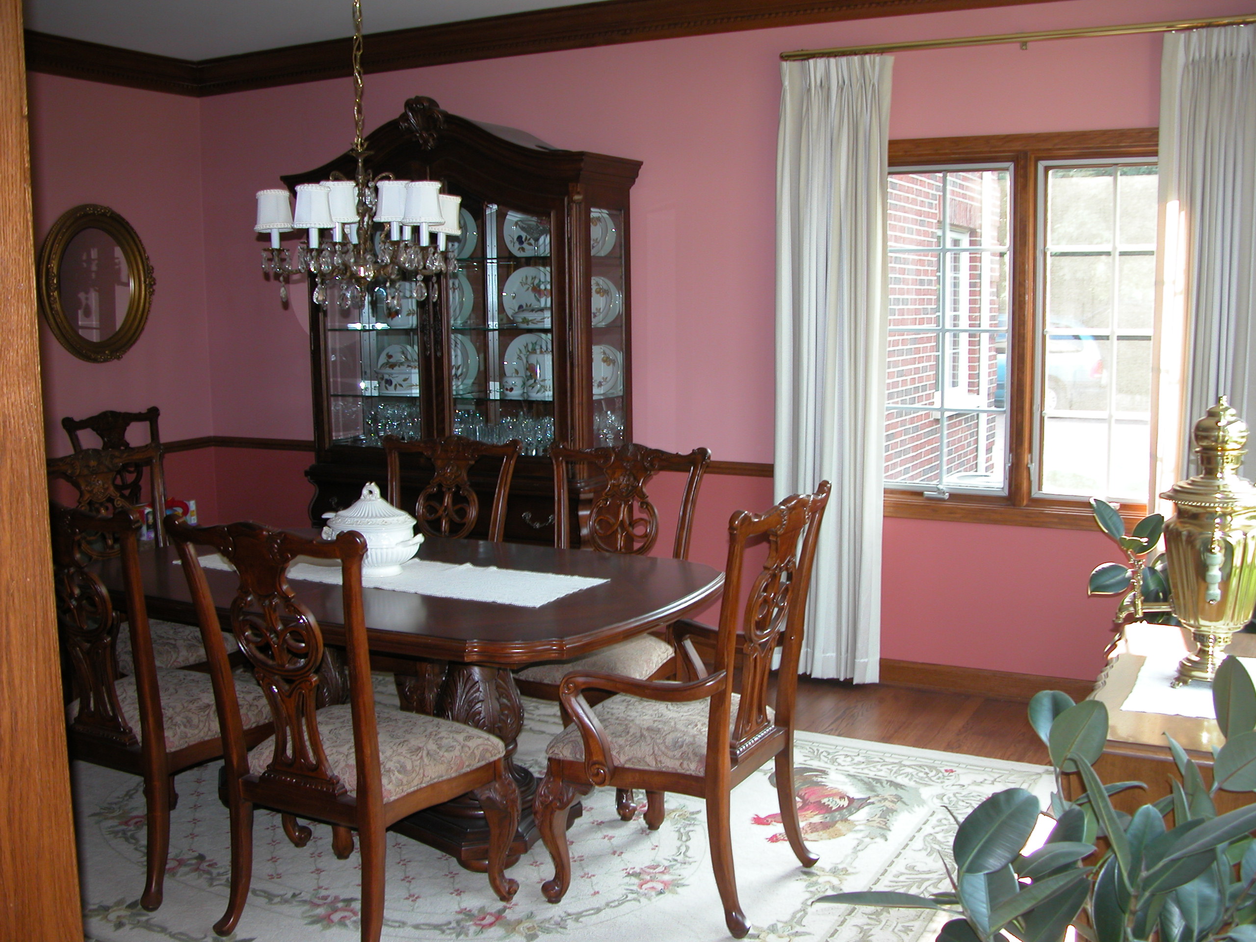 Formal dining room with rose-colored walls, traditional dark wood furniture, and a crystal chandelier